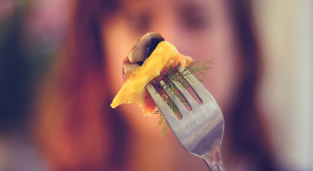 Woman holding a fork with food up in front of her face